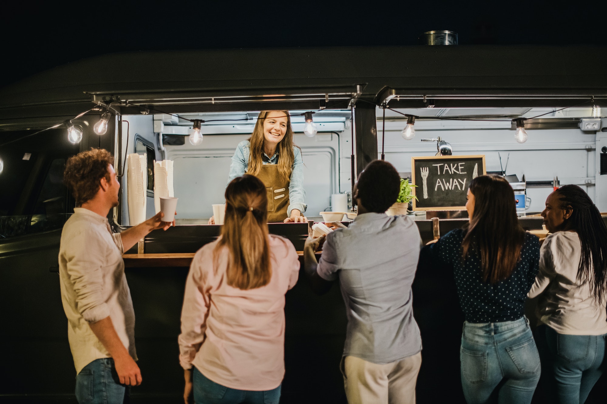Diverse clients speaking with food truck seller at night